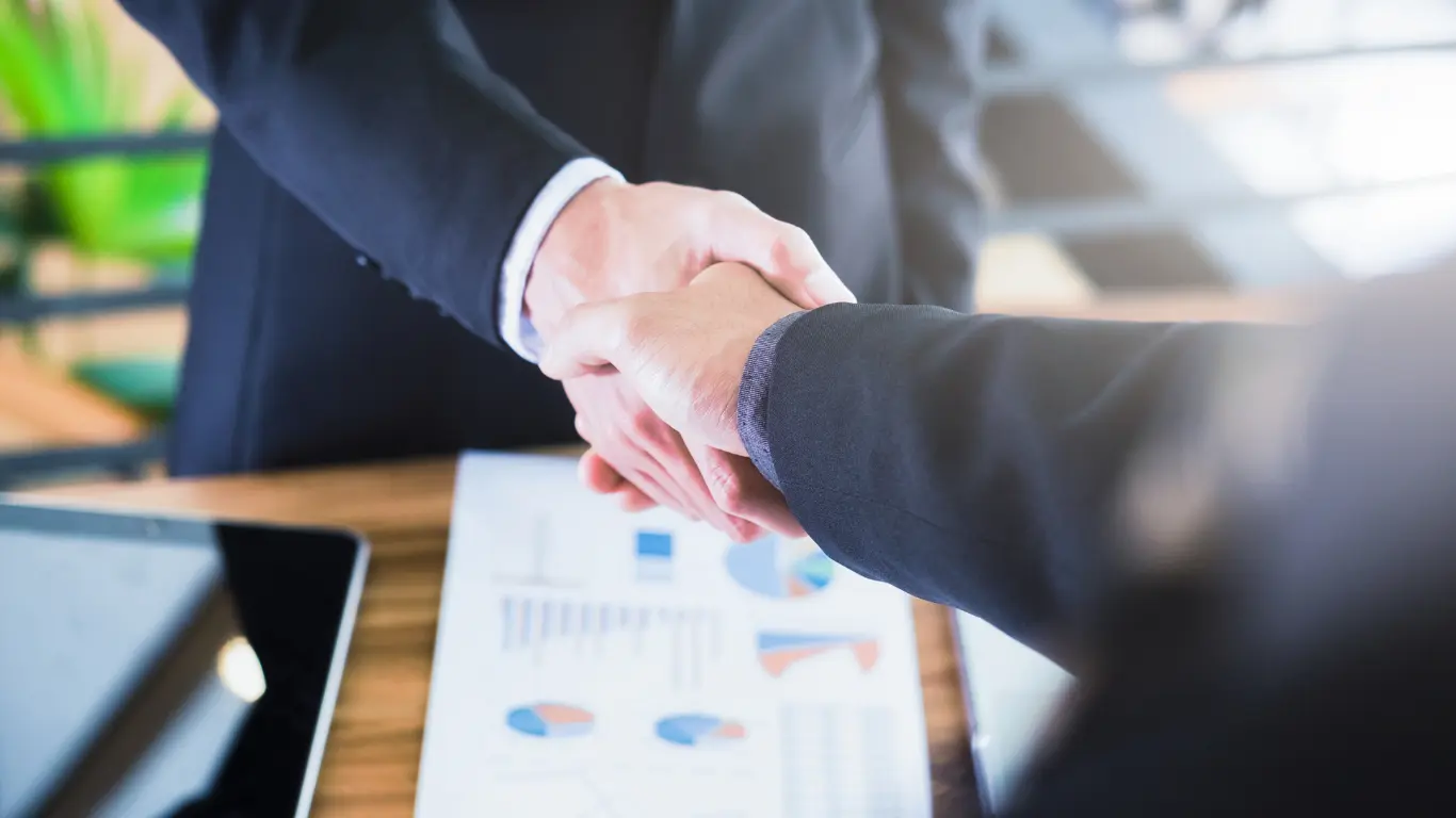 Business leaders shaking hands over performance reports, representing strategic digital partnerships for B Corp growth