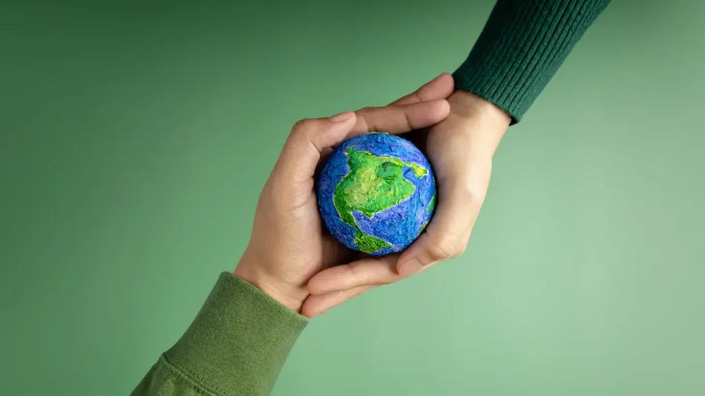 Hands gently holding a small Earth globe against a green background, symbolizing sustainable digital marketing strategies, shared responsibility, and purpose driven brand growth.