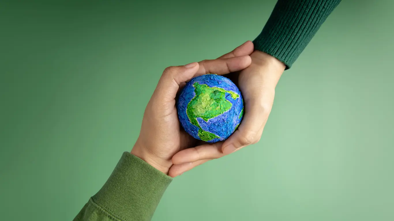 Hands gently holding a small Earth globe against a green background, symbolizing sustainable digital marketing strategies, shared responsibility, and purpose driven brand growth.