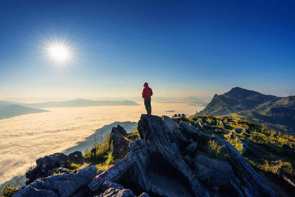 A person standing on a mountain ridge above the clouds at sunrise