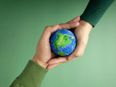 Hands gently holding a small Earth globe against a green background, symbolizing sustainable digital marketing strategies, shared responsibility, and purpose driven brand growth.
